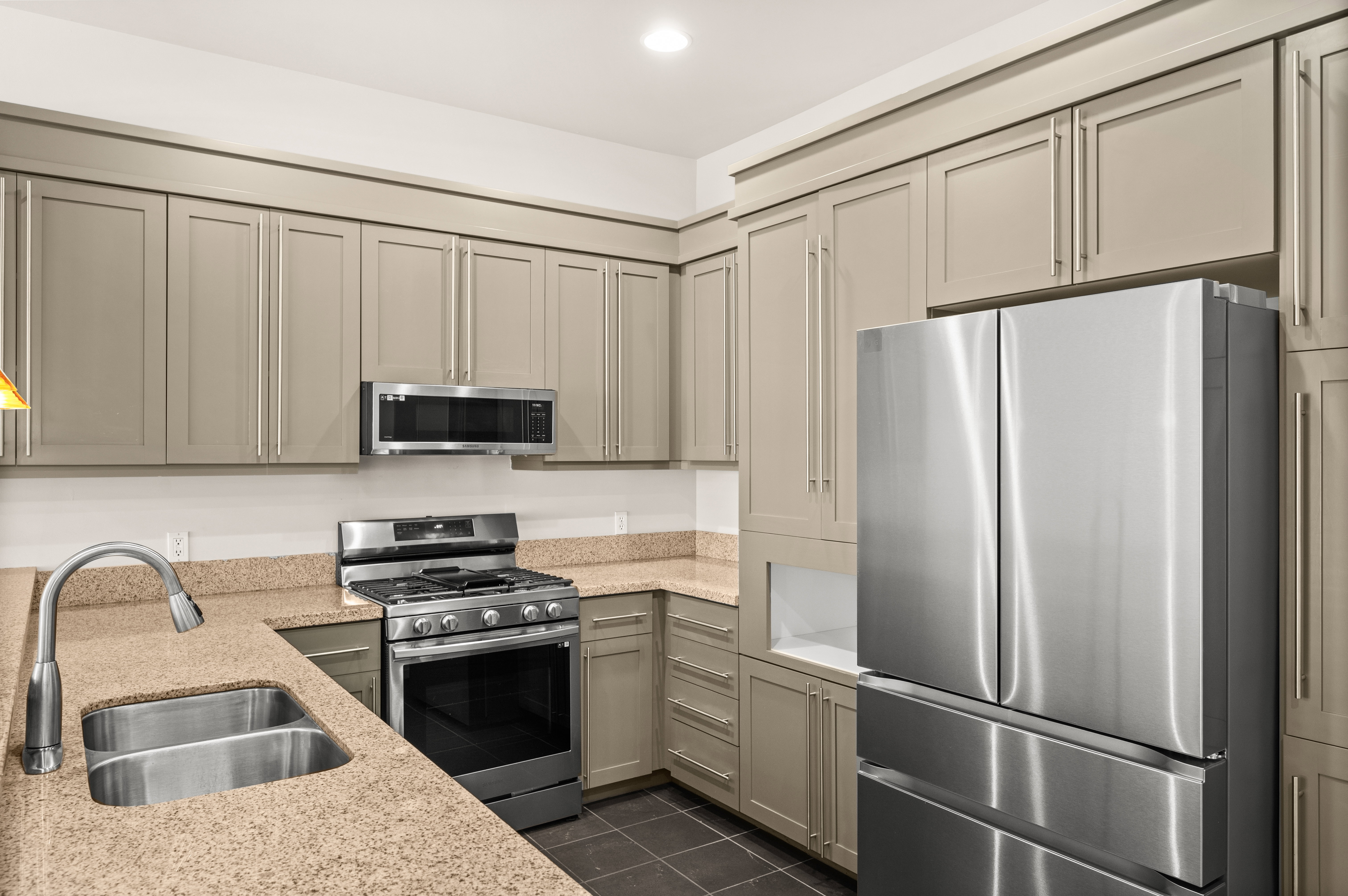 Kitchen featuring full-height cabinetry, stainless steel appliances, speckled countertops, a double basin sink, and dark tile flooring