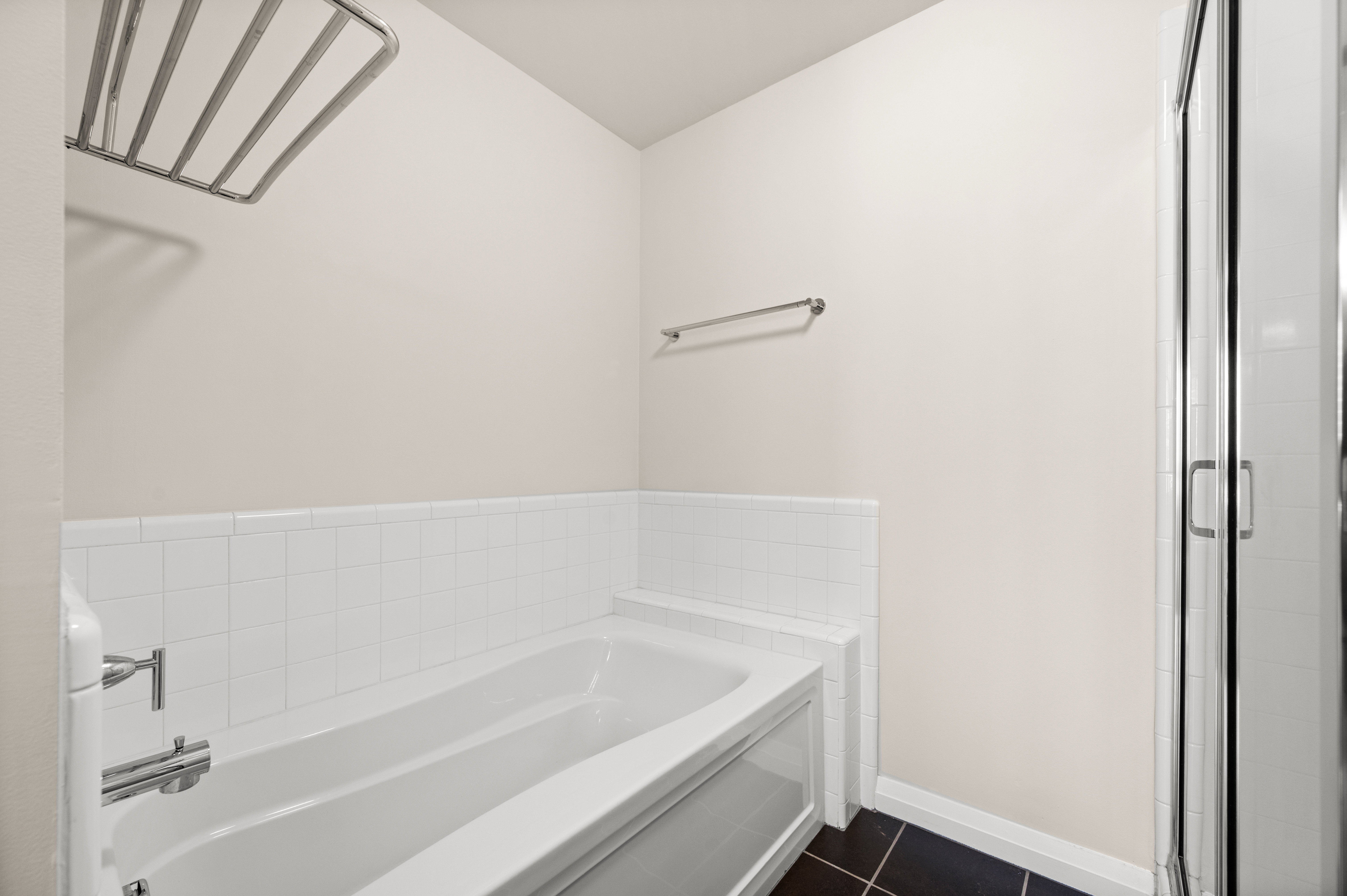 Bathroom featuring a white bathtub, subway tile wainscoting, and dark tile flooring