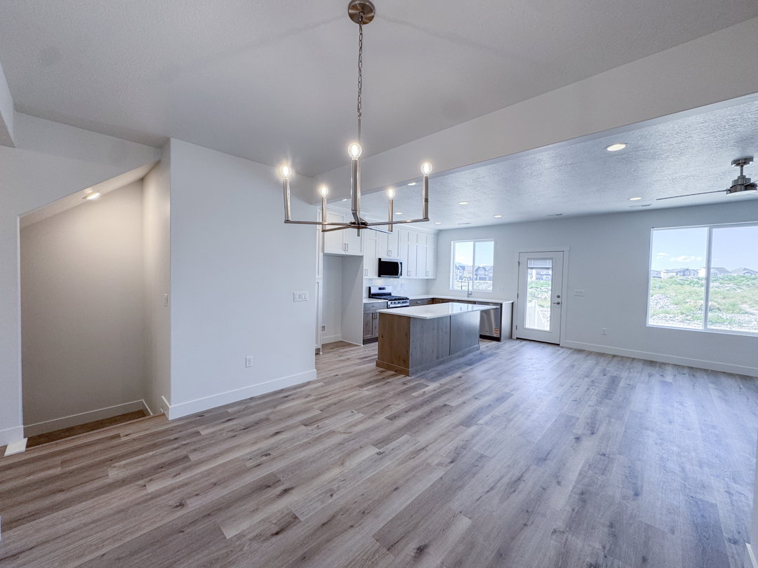 Open-concept living space featuring wood-finish flooring, a modern kitchen with a large island, white cabinetry, and stainless steel appliances
