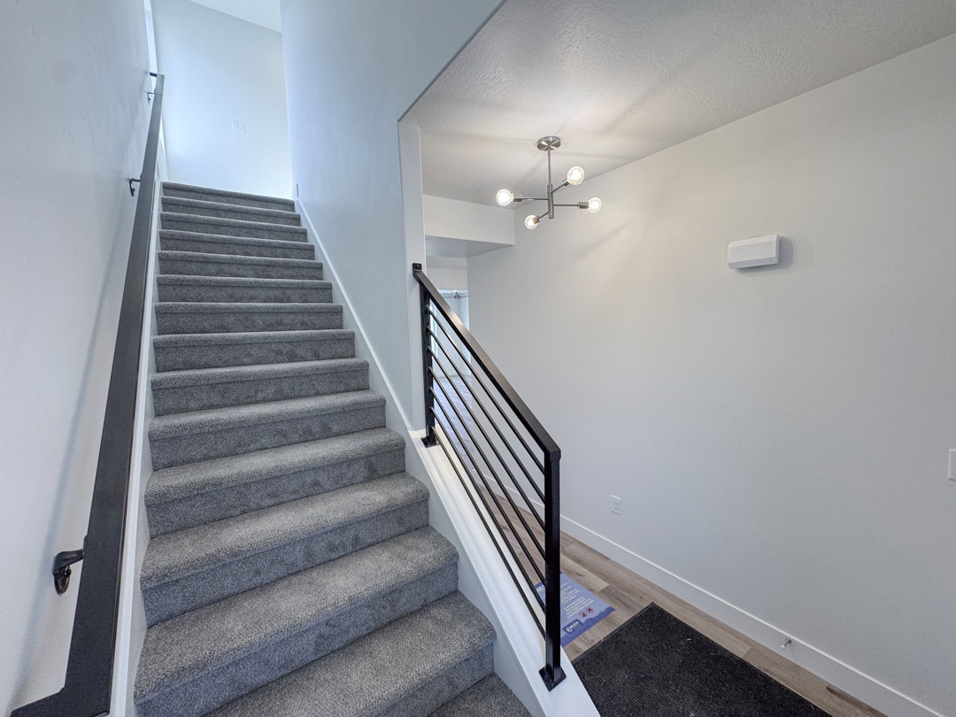 Carpeted staircase with contemporary horizontal metal railings and a coordinating wall-mounted handrail