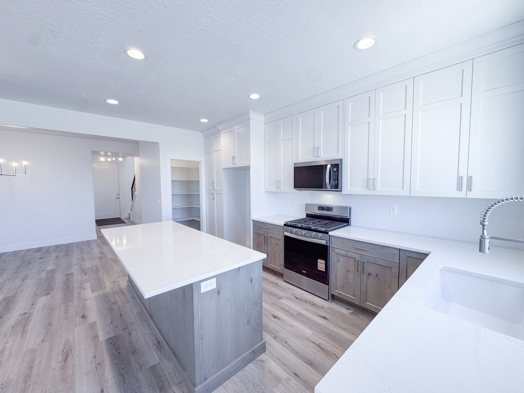 Modern kitchen featuring a large center island, white shaker cabinetry, stainless steel appliances, and wood-finish flooring