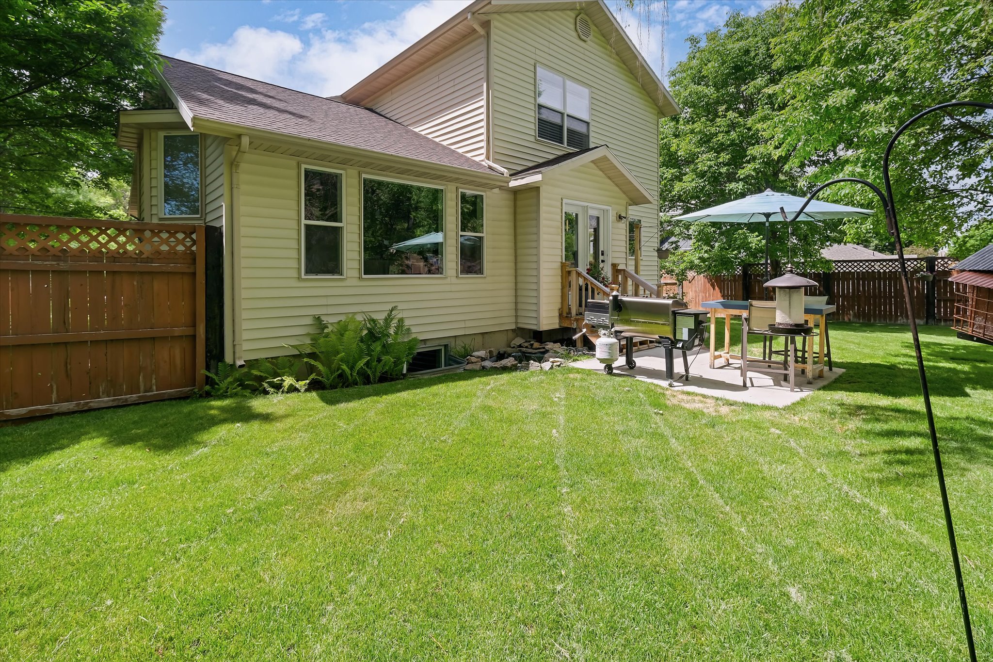 Expansive backyard featuring a lush lawn, privacy fencing, and a concrete patio