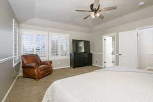 Carpeted room featuring multiple windows with white plantation shutters, a vaulted ceiling, and a ceiling fan with light kit