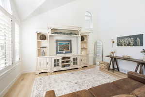 Vaulted ceilings featuring a high arched window, wood-finish flooring, plantation shutters, and a built-in media center with shelving