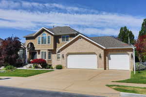Stucco and brick facade with an arched entry, a two-car garage, multiple gabled rooflines, and a well-maintained front lawn
