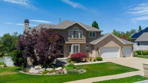 Stucco and brick exterior featuring an arched entryway, multiple windows including an arched window, a two-car garage, and landscaped front yard with mature trees