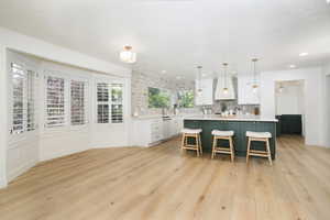 Open-concept kitchen and dining area featuring light wood-finish flooring, a kitchen island with seating, pendant lighting, white cabinetry, and a stone accent wall