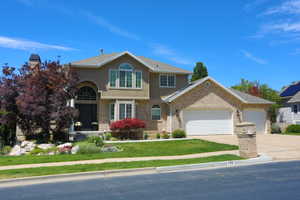 Stucco and brick exterior with a prominent arched entry, multiple multi-pane windows, an attached two-car garage, and mature landscaping