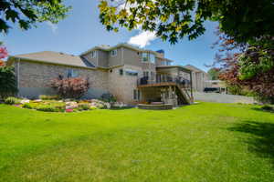 Expansive lawn area featuring a multi-level deck, a built-in outdoor seating area, a landscaped rock garden, and a brick and siding exterior