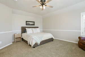Carpeted interior space featuring tray ceiling, ceiling fan with integrated lighting, two-tone painted walls with chair rail molding, and window with plantation shutters