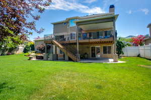 Spacious backyard featuring a multi-level deck, a lower patio, a stone fire pit area, and a white privacy fence