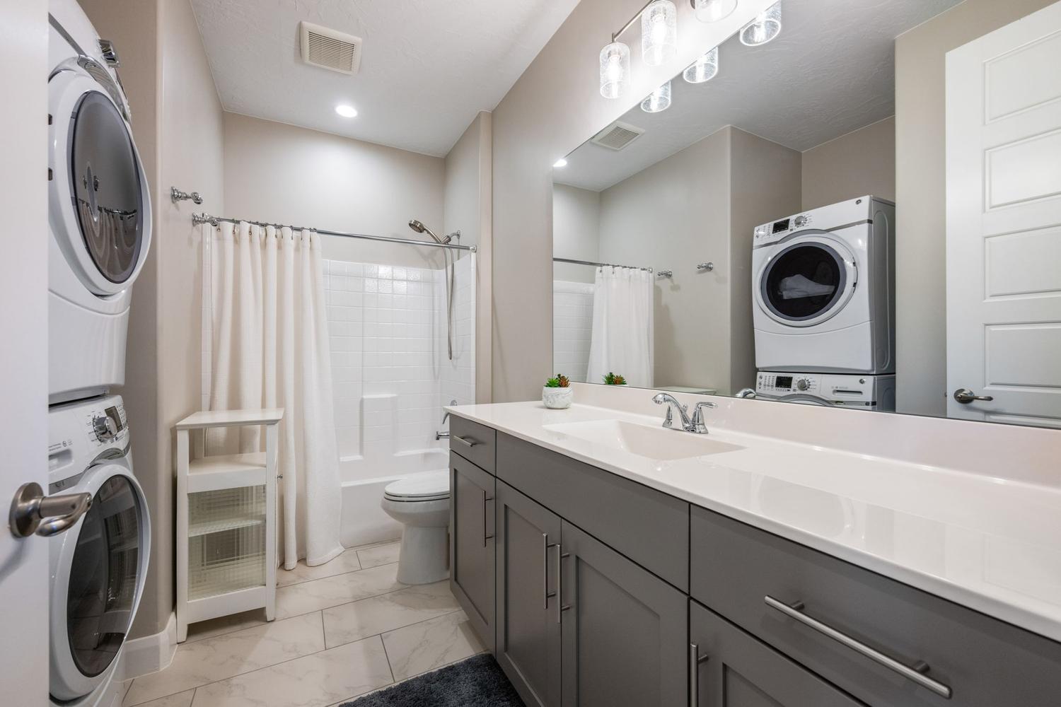 Well-appointed bathroom featuring a spacious vanity with a white countertop and gray cabinetry, a full-width mirror, and a modern light fixture