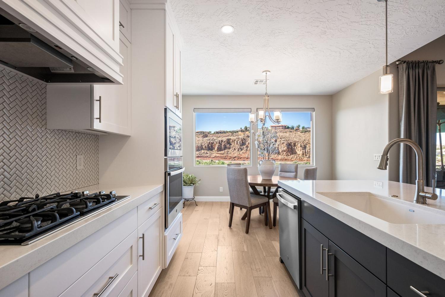 Modern kitchen featuring light cabinetry, herringbone tile backsplash, built-in ovens, gas cooktop, and a peninsula with an undermount sink