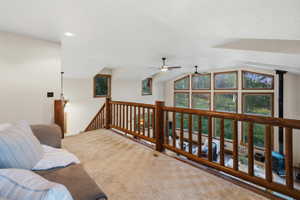 Carpeted loft space featuring natural wood railing and a wall of windows