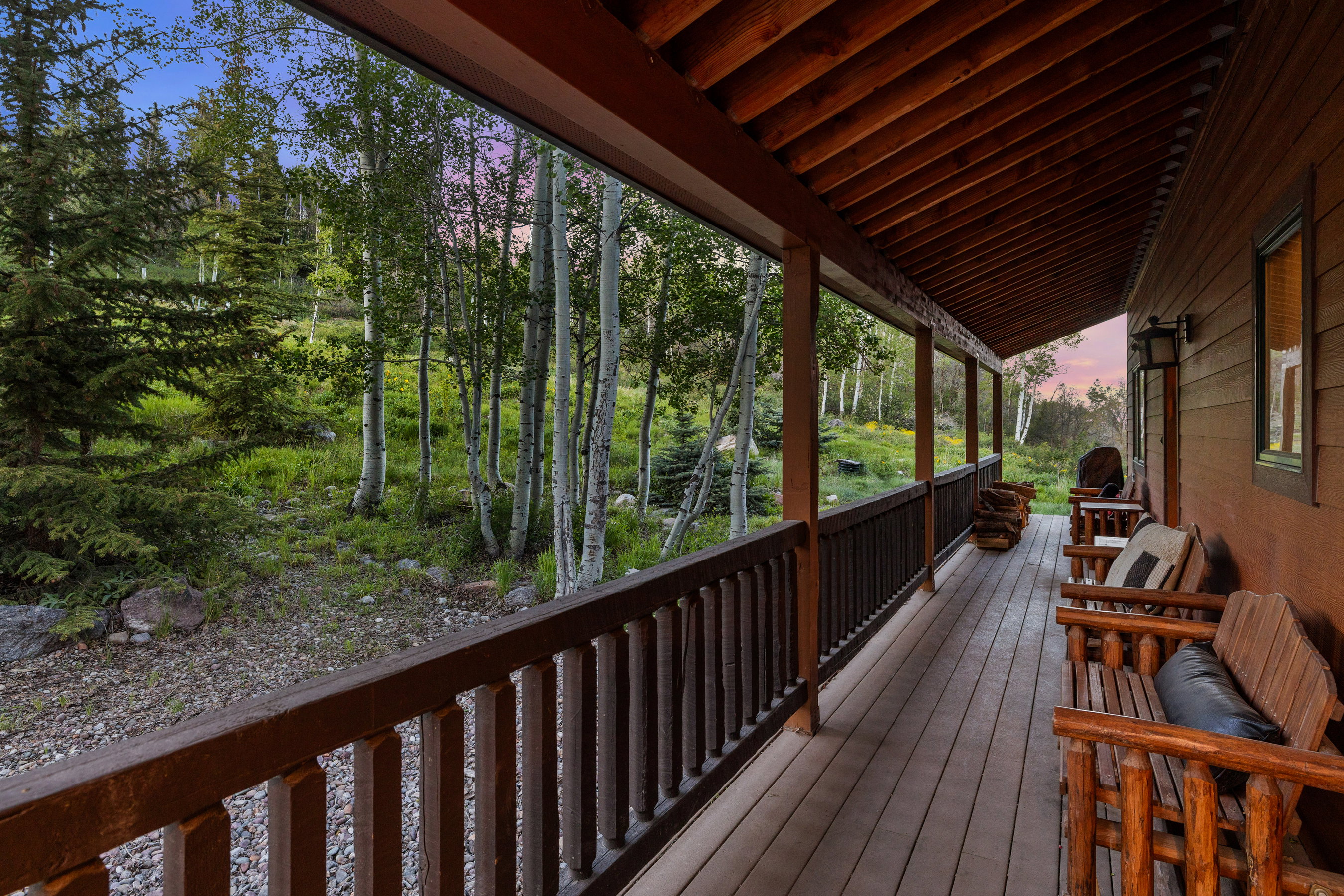 Expansive covered porch featuring wood-finish decking, dark wood railings, and exposed wood ceiling beams