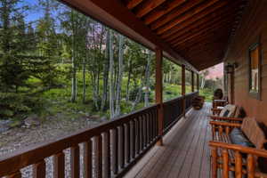 Expansive covered porch featuring wood-finish decking, dark wood railings, and exposed wood ceiling beams