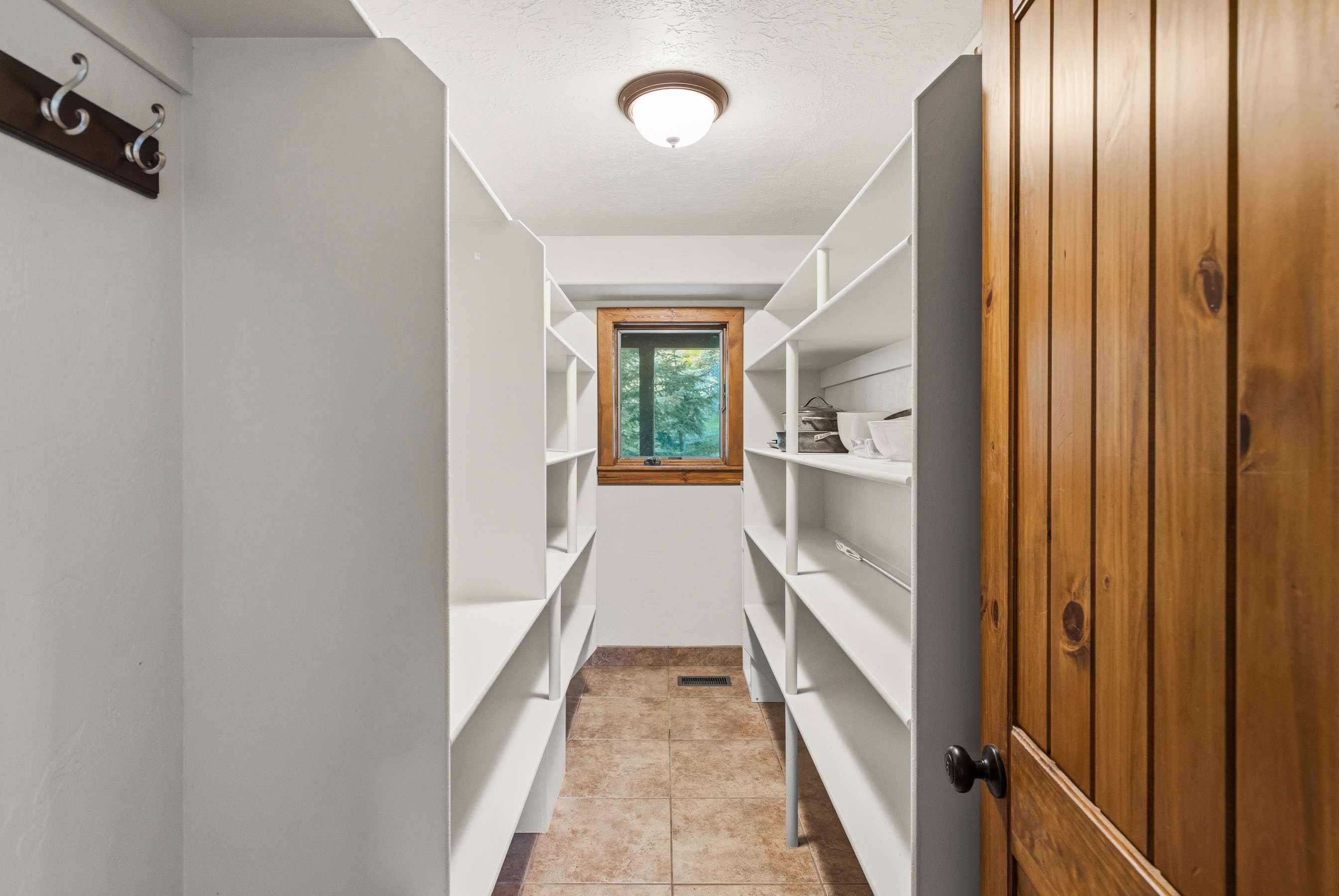 Spacious walk-in pantry featuring extensive white shelving, a wood-framed window, recessed ceiling light fixture, and tile flooring