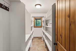 Spacious walk-in pantry featuring extensive white shelving, a wood-framed window, recessed ceiling light fixture, and tile flooring