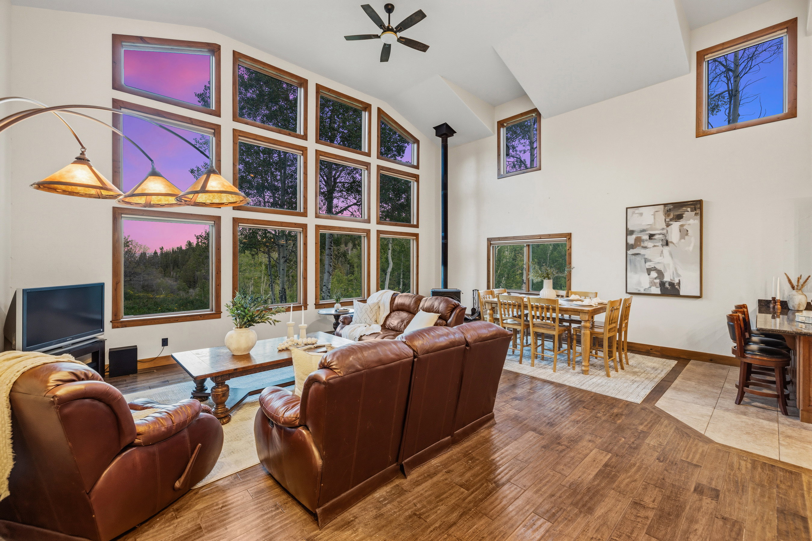 Expansive living area featuring vaulted ceilings, a prominent wood-burning stove, and a wall of multi-pane windows providing natural light