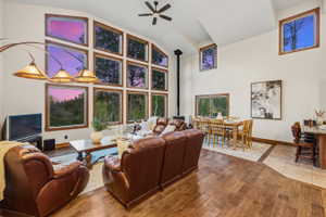 Expansive living area featuring vaulted ceilings, a prominent wood-burning stove, and a wall of multi-pane windows providing natural light