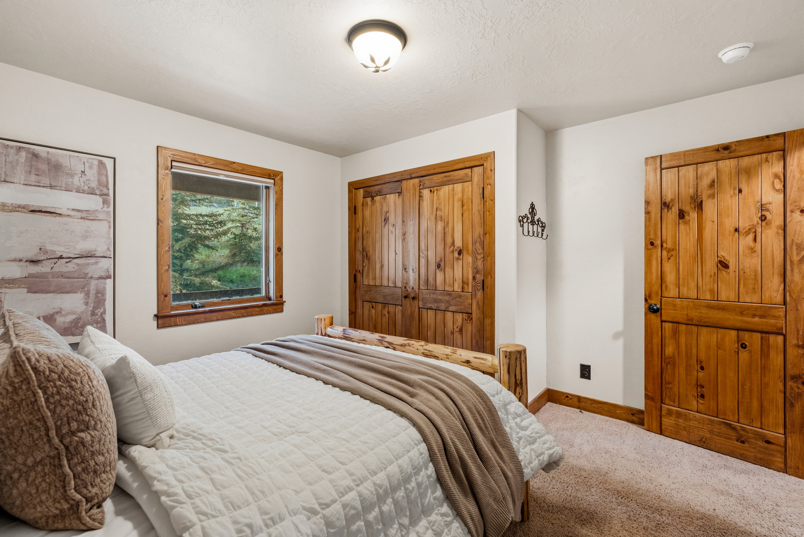 Bedroom featuring wood-finish doors and window trim, a carpeted floor, and a window overlooking exterior greenery