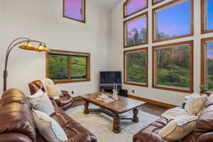 Two-story vaulted ceiling living area featuring a wall of multiple large windows, wood-finish flooring, and a substantial wood-frame window system