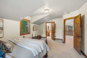 Room featuring sloped ceilings, a window with natural wood trim, light-toned carpeting, and natural wood doors