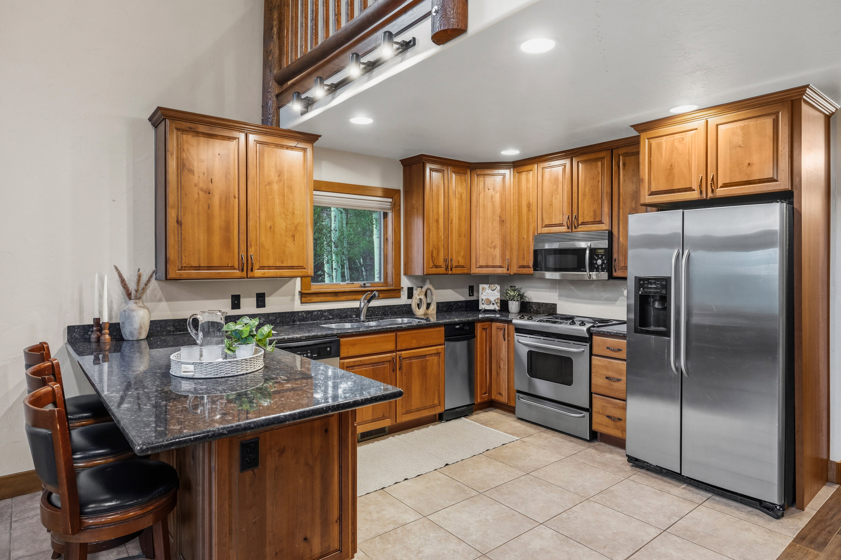 Kitchen featuring wood cabinetry, stainless steel appliances, granite countertops, and tile flooring