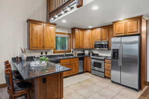 Kitchen featuring wood cabinetry, stainless steel appliances, granite countertops, and tile flooring