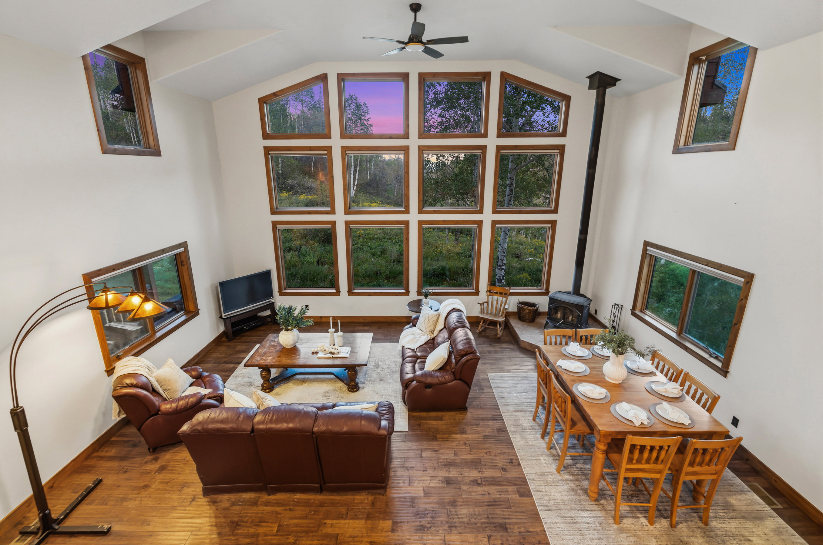 Vaulted ceiling living area featuring wood-finish flooring, a wood-burning stove, and a wall of multi-pane windows