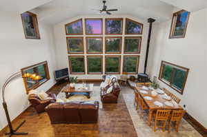 Vaulted ceiling living area featuring wood-finish flooring, a wood-burning stove, and a wall of multi-pane windows
