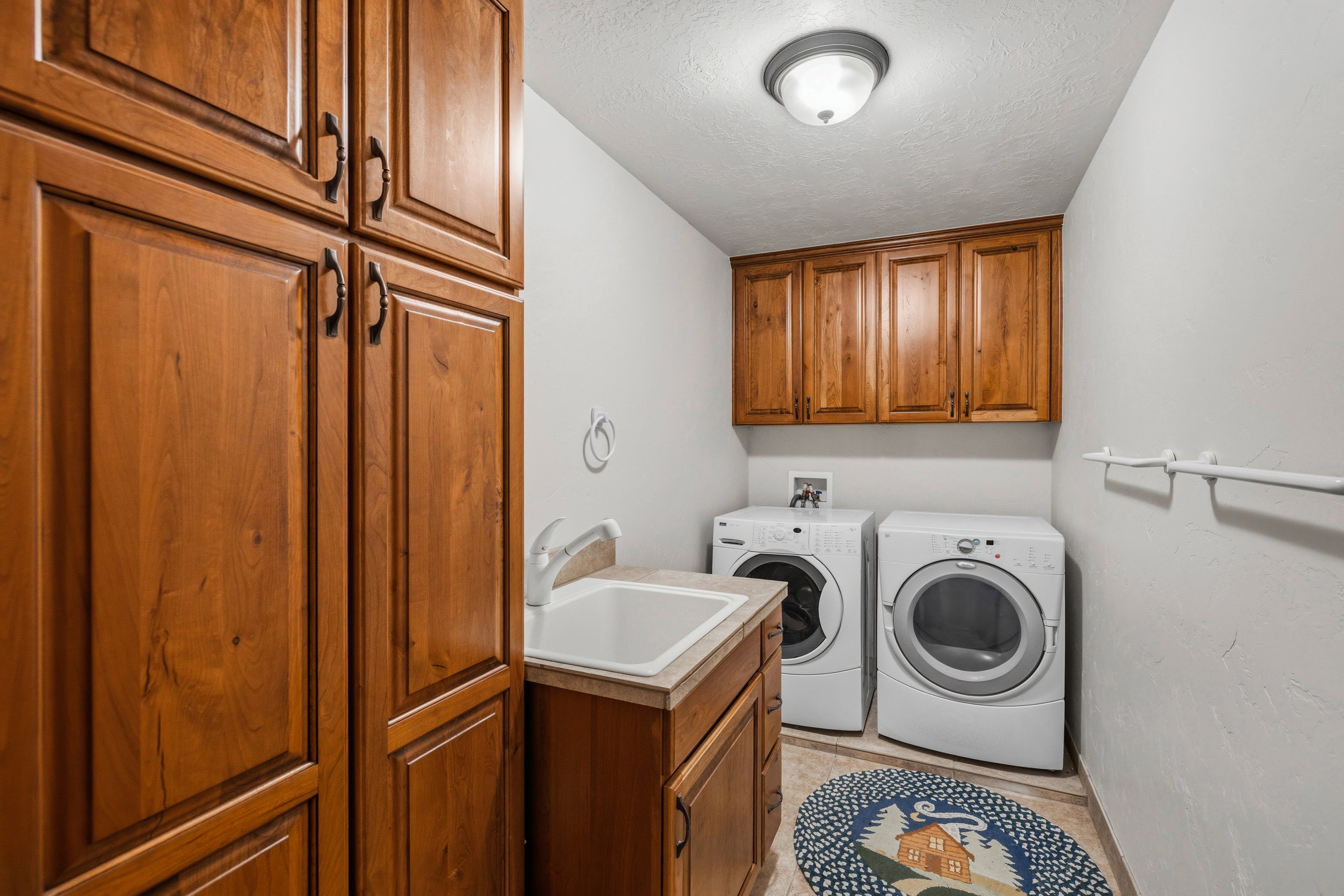 Dedicated laundry area featuring ample wood-finish cabinetry, a utility sink with a laminate countertop, and overhead lighting
