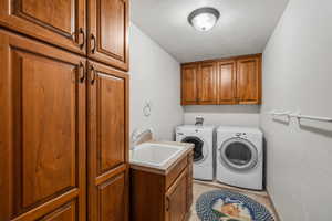 Dedicated laundry area featuring ample wood-finish cabinetry, a utility sink with a laminate countertop, and overhead lighting