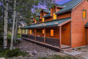 Wood-sided exterior featuring a covered porch with a railing, multiple dormer windows, and a dark green metal roof
