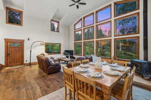 Vaulted ceiling living and dining area featuring a full wall of picture windows, wood-finish flooring, and a wood-paneled entry door with transom