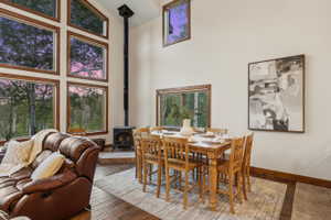 Expansive wood-framed windows, a corner wood-burning stove with a stone hearth, and a high vaulted ceiling define this interior space