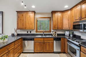 Kitchen featuring wood cabinetry, dark countertops, stainless steel appliances, and a window above the sink
