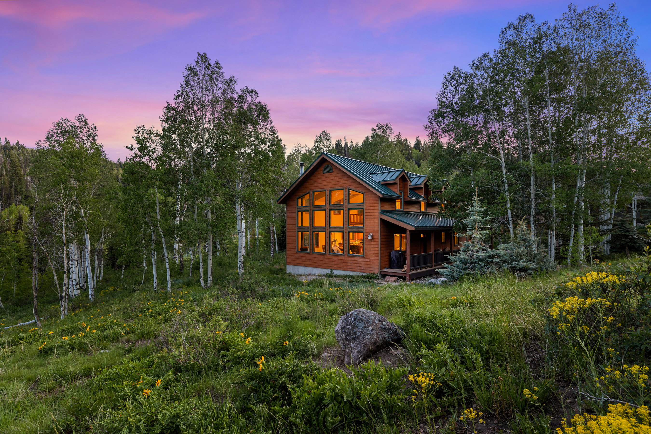 Log cabin exterior with a green metal roof, multiple dormer windows, and a covered porch