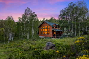 Log cabin exterior with a green metal roof, multiple dormer windows, and a covered porch