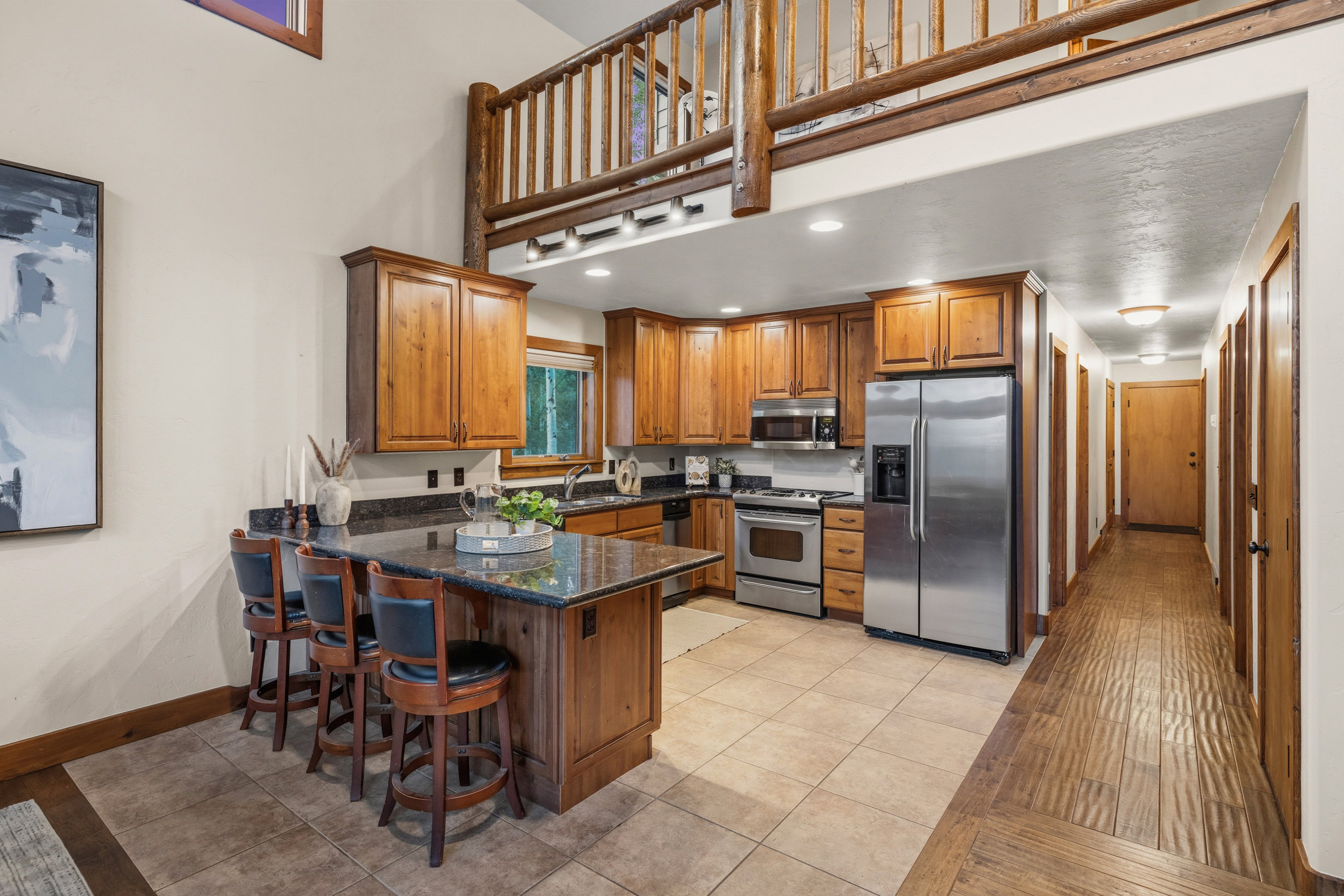 Kitchen featuring wood cabinetry, stainless steel appliances, dark countertops, and a breakfast bar with seating for three
