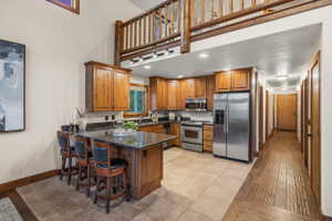Kitchen featuring wood cabinetry, stainless steel appliances, dark countertops, and a breakfast bar with seating for three