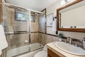 Bathroom featuring a tiled shower/tub combination with glass enclosure, a window, a wood-framed mirror, and a vanity with an integrated sink and chrome fixtures