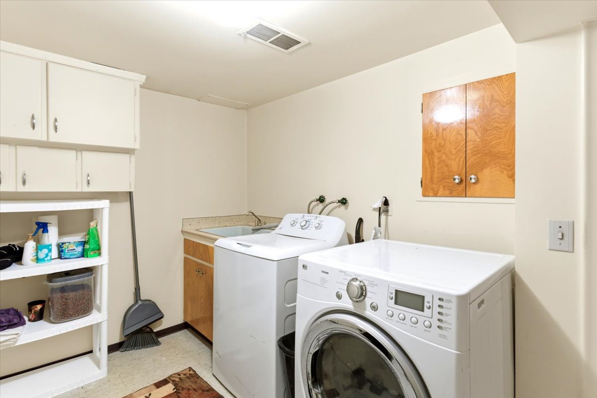 Dedicated utility space featuring a laundry sink, wood-finish cabinetry, upper storage cabinets, built-in shelving, and light-toned walls