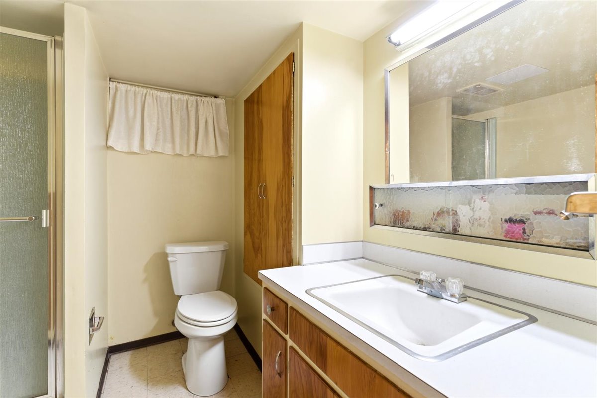 Bathroom featuring a white vanity with an integrated sink, a large wall-mounted mirror, and an adjacent shower enclosure with a clear glass door