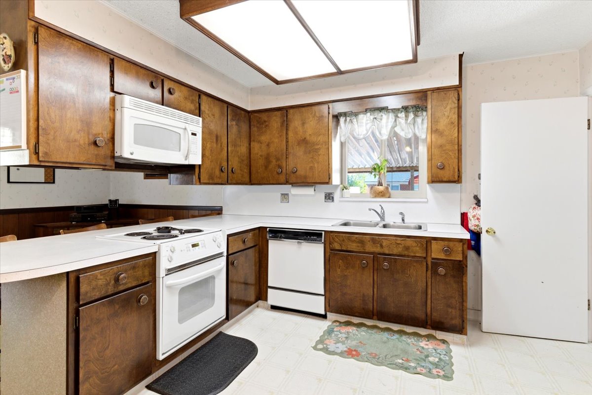 Kitchen featuring wood cabinetry, white countertops, built-in white appliances, and a double basin sink