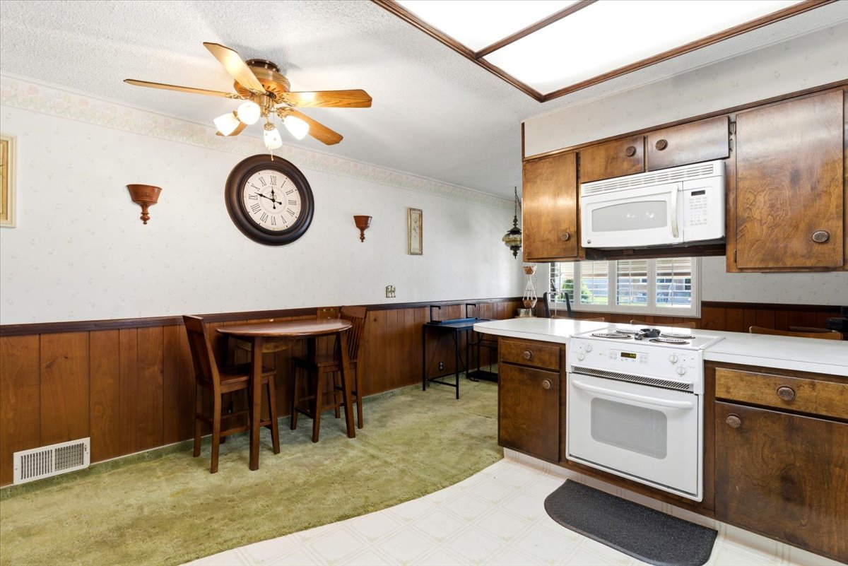 Kitchen area featuring rich wood-finish cabinetry, white countertop surfaces, and a white electric range with a coordinating microwave