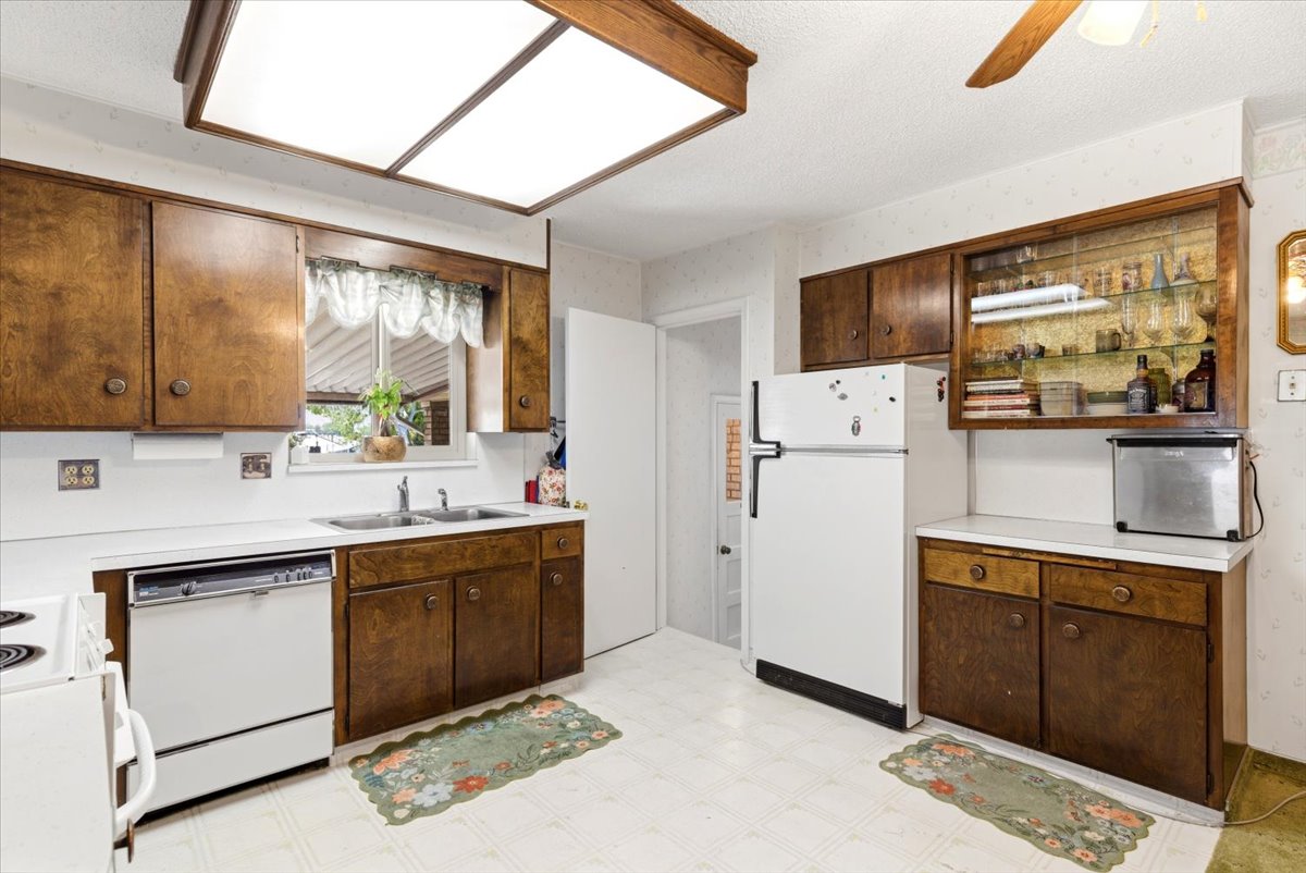 Kitchen featuring wood cabinetry, white countertops, a double basin sink, and a built-in dishwasher