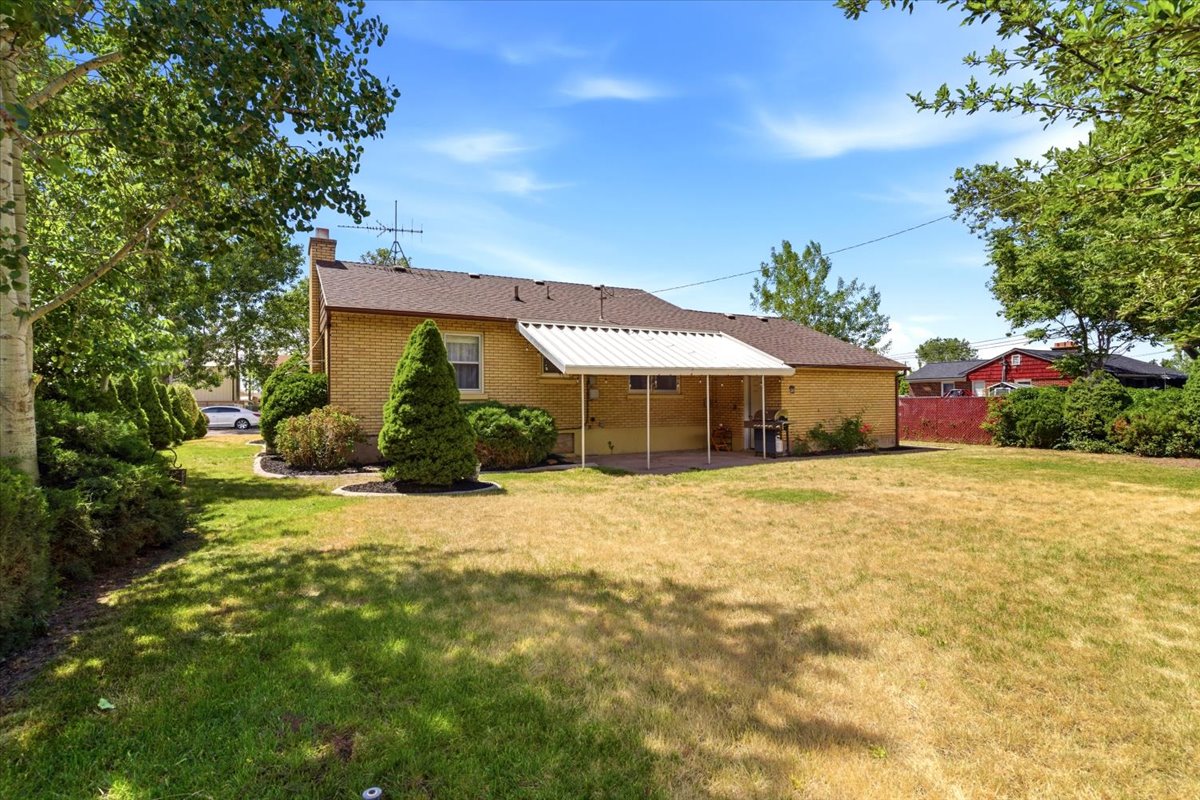 Expansive rear yard featuring mature perimeter trees, a covered patio, and a brick exterior with a pitched roof