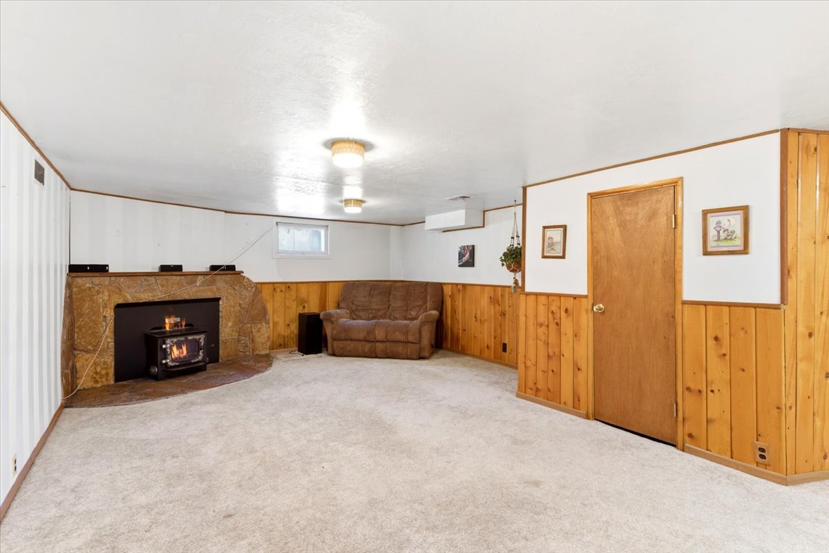Carpeted room featuring a stone fireplace with a wood-burning stove insert, wood paneling, and white painted walls