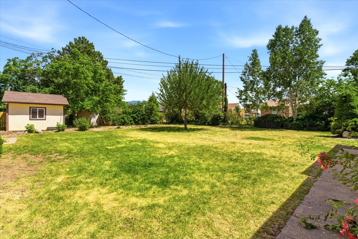 Spacious backyard featuring a manicured lawn, established trees, and a detached storage shed with a shingle roof
